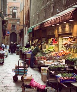 Narrow cobblestone street in Bologna's Quadrilatero market, lined with vibrant fruit and vegetable stalls
