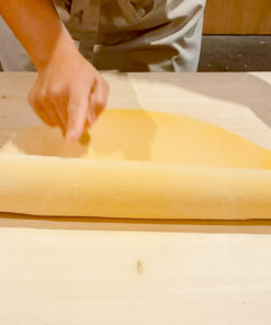 Traditional Italian pasta making: Chef or student stretching fresh egg pasta dough by hand with a rolling pin