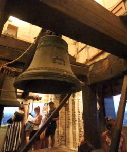 Visitors inside a historic Bologna Cathedral bell tower, admiring large bells and the city view