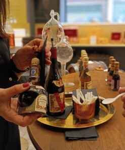 Close-up of hands holding a bottle of Giuseppe Giusti balsamic vinegar and a tasting spoon in Modena.